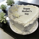 A white two layer cake with Happy Mother's Day in frosting on the top.