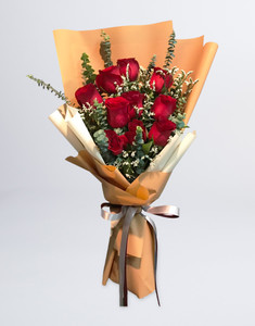 ผู้หญิงถือช่อดอกไม้ที่จัดด้วยดอกกุหลาบสีแดง 12 ดอก ห่อกระดาษสีส้มชานม ผูกริบบิ้นสีแดงและสีขาว