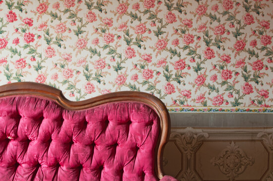 Red couch in an antique house in front of a flower design wallpaper