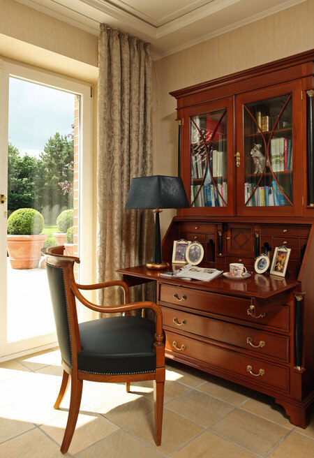 a wooden antique secretary desk with multiple drawers near a wooden leather chair