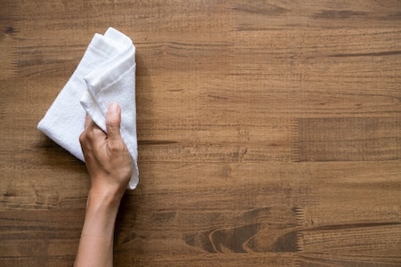 person wiping down a wood furniture table with a dry cloth