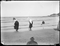 Dipping toes in water â€“ frilly bonnets â€“ little child kicking up leg â€“ photographerâ€™s shadow in foreground.