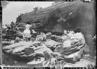 Children sitting and changing on Rocks at Coogee â€“ clothes spread all about below sandstone wall.