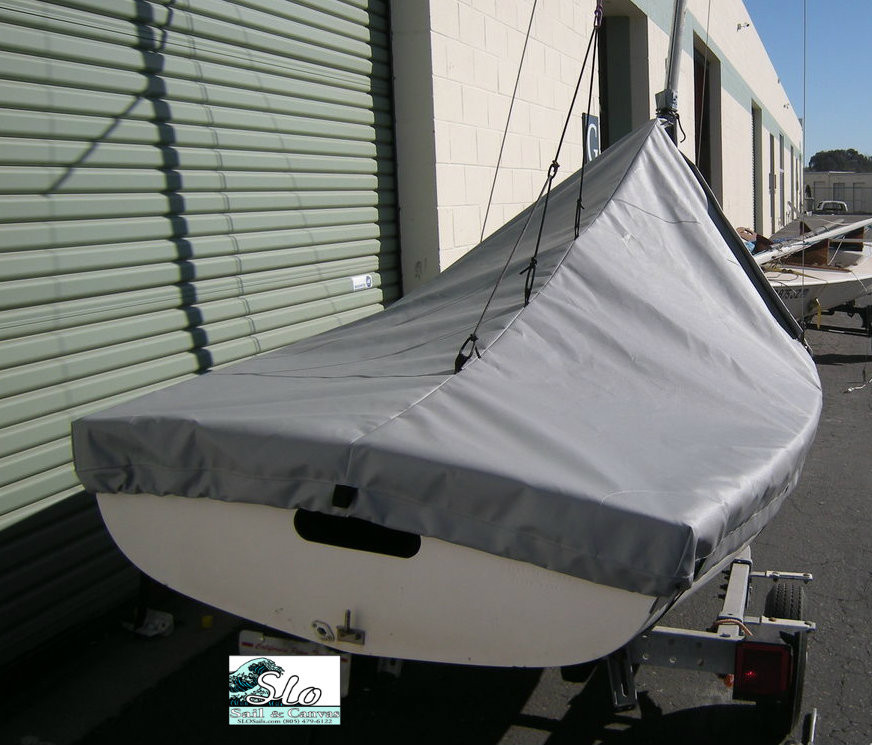 Flying Junior sailboat Mast Up Peaked Mooring Cover by SLO Sail and Canvas. 1/4" shockcord is built into cover to secure your cover tightly around the boat's rubrail. Web Loops allow you to “tent” your cover up to prevent pooling of water. Reinforcements positioned over blocks and cleats prevent chafing.

