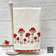 Mushrooms with red cap and white spots embroidery border design on ecru kitchen cotton towel and red trim at bottom hem.  
