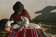 A Bolivian woman weaves brightly colored fabric on a loom