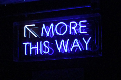 Blue fluorescent sign reading 'More this way' with an arrow pointing upwards