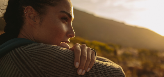 Woman sits outdoors looking thoughtfully up at the trees