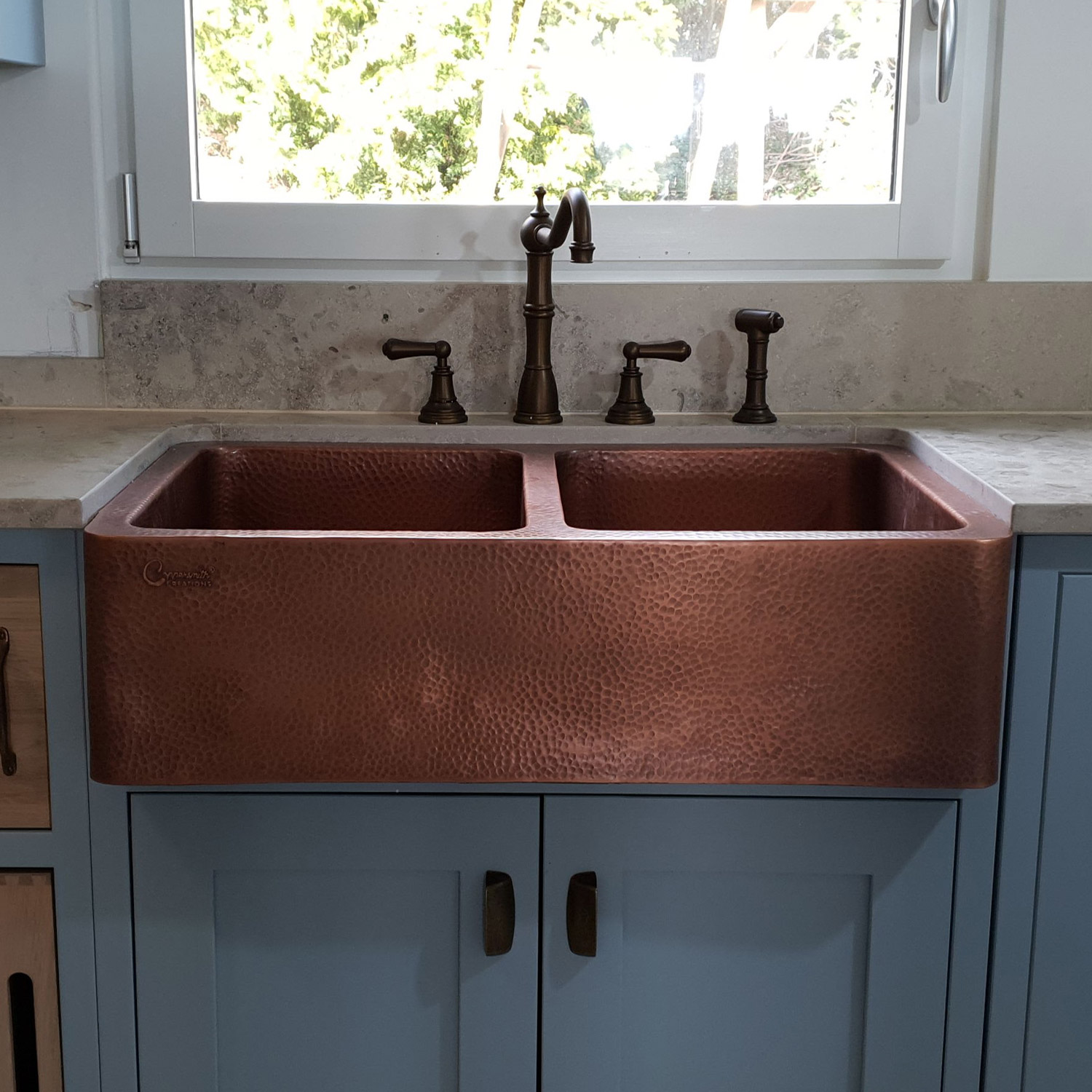 large copper sink with two bowls installed in a rustic kitchen