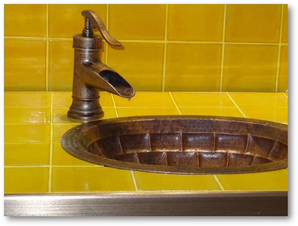 hammered copper sink installed in a bathroom counter with mexican tiles