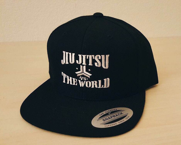 OGA Open Guard Apparel Jiu Jitsu vs The World Snapback hat.  black hat with white embroidery in the background of his picture..  Jiu Jitsu vs the world series from Open guard apparel. 

Enjoy Free Shipping on all products storewide today. 
