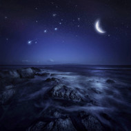 Rising Moon Over Ocean And Boulders Against Starry Sky