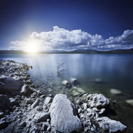 Tranquil Lake And Rocky Shore With Sun Over Horizon Sardinia Italy