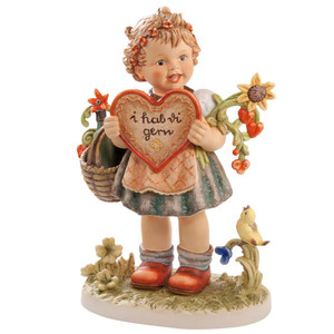 The 13-inch M.I. Hummel 'Valentine Gift' Masterpiece (HUM 387/III) features a girl with baskets of flowers and a songbird. Close-up of the intricately sculpted flowers and the soft, authentic painting style of the Masterpiece Valentine Gift.