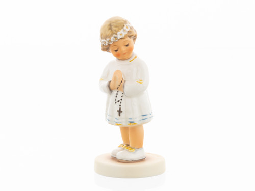 The traditional M.I. Hummel 'Peaceful Blessing' figurine (HUM 814) featuring a girl in a white dress holding a communion candle. A close-up of the delicate floral details and the serene facial expression of the girl in Peaceful Blessing.