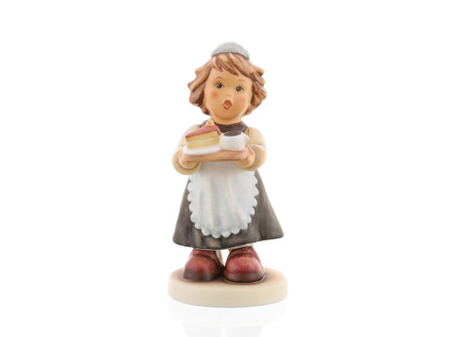 A close-up of the delicate porcelain tray, the hand-painted slice of cake, and the girl’s traditional apron and headpiece. M.I. Hummel 'Maid to Order' (HUM 2091) featuring a young girl in a black and white maid uniform carrying a tray with a teapot and cake.