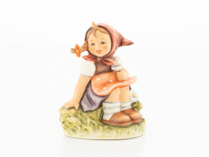 M.I. Hummel figurine HUM 459 of a girl sitting in a meadow picking flowers.