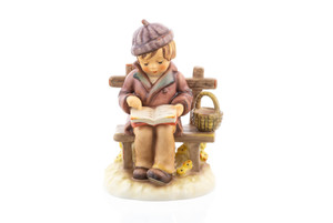 M.I. Hummel figurine HUM 464 Young Scholar featuring a child with a purple hat sitting on a bench reading a book, handcrafted in Germany.