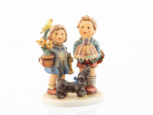 M.I. Hummel 90th Anniversary Limited Edition HUM 763 figurine of a boy with cake, a girl with a flower and bird, and a dog looking at the cake.