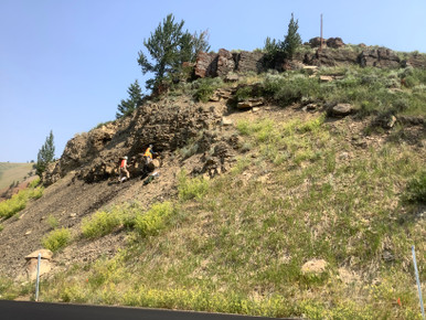 Two geologists stand on a slope at the bottom of a roadcut along Gros Ventre Road. They are looking at the contact between the Retort and Tosi Chert members of the Permian Phosphoria Formation.