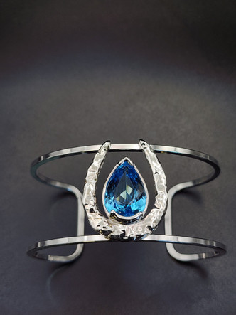 Stunning hammered horseshoe bracelet in sterling silver featuring a pear Swiss blue topaz. A true statement piece for your wardrobe.