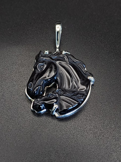 A unique black obsidian carved mare and foal pendent. This stone is set in sterling silver with a unique paisley pattern design on the reverse side in the silver. It will pick up unique colors in the sunlight. This pendant resembles a Friesian mare and foal.