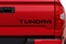 Rear tailgate of red Toyota Tundra truck showing black letter and text decals.