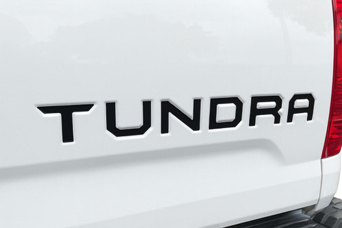 Rear tailgate of white Toyota Tundra truck showing black letter and text decals.