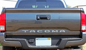 Rear tailgate of dark Toyota Tacoma truck showing silver letter and text decals.