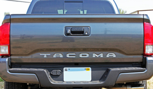Rear tailgate of dark Toyota Tacoma truck showing silver letter and text decals.