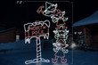 Animated LED sign of four green and red elves stacked on top of one another hammering a red and white "North Pole" sign into the ground with dimensions 7'2" by 9'10"