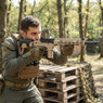 A person aiming the Vorsk VMP-2MD GBB Airsoft Rifle in Tan (300FPS-Fixed Semi Auto) in a wooded outdoor setting A person aiming the Vorsk VMP-2MD GBB Airsoft Rifle in Tan (300FPS-Fixed Semi Auto) in a wooded outdoor setting