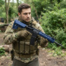 A tactical airsoft player holding the Cyma CM615 AEG Keymod hand-guard Rifle In blue in a forest setting. A tactical airsoft player holding the Cyma CM615 AEG Keymod hand-guard Rifle In blue in a forest setting.