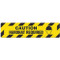 Photograph of an anti-slip floor safety sign reading "Caution Hardhat Required" in black on a yellow background.  Includes a graphic of a head wearing a hardhat.