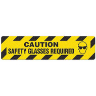 Photograph of an anti-slip floor safety sign reading "Caution Safety Glasses required" in black on a yellow background.  Includes a graphic of a face with safety glasses.