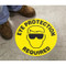 A photograph of the yellow "EYE PROTECTION REQUIRED"  Slip-Gard™ Floor Sign on the floor with a person's boots standing near.