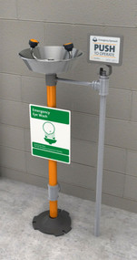 A photograph of a Guardian GFR1825 Freeze-Resistant Eyewash, Pedestal Mounted, Stainless Steel Bowl installed next to a cinderblock wall.