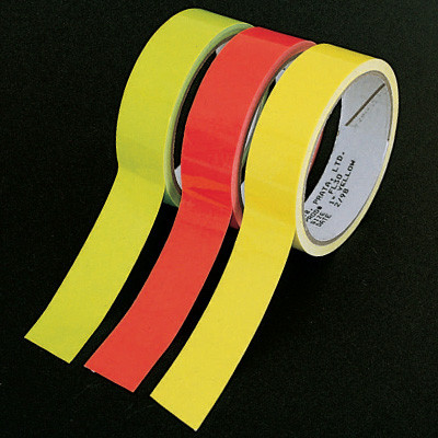 A photograph of three rolls of 06474 fluorescent tape with a several inches extended from each. Left to right: green, orange, yellow.