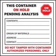 A photograph of a red and white 12327 waste label, reading this container on hold pending analysis, with graphic.