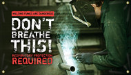 Picture of Workplace Safety Banner that features a metal workshop as background. In the front is a worker with a face-guard to protect himself welding a piece of metal. There are fumes coming off this welding job. On the left side of the banner there is a red stripe at the top, with words cut out that reads "Welding fumes are dangerous". Below that is large white text that reads "Don't breathe this!". Finally below that in alert red text it reads "Respiratory protection required".