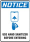 A photograph of a blue and white 03445 OSHA notice sign, reading use hand sanitizer before entering, with icon.