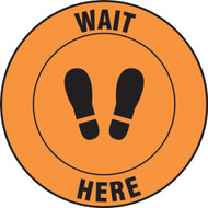 A photograph of an orange and black 11236 social distance floor sign, reading wait here with footprints icon.