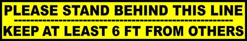 A photograph of the yellow and black 05421 please stand behind this line | KEEP AT LEAST 6 FT FROM OTHERS, removable social distance floor sign.