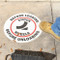 A picture of a "Chock wheels before loading/before unloading" pavemebt sign installed on  a concrete surface with a person's foot and wheel chock nearby.