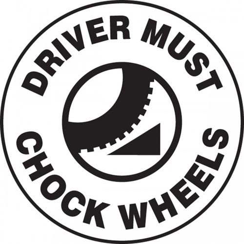 This black and white sign features the text "Driver Must Chock Wheels". The center shows the image of a chock being actively used on a wheel. Use to prevent accidents caused by uncontrolled vehicles.