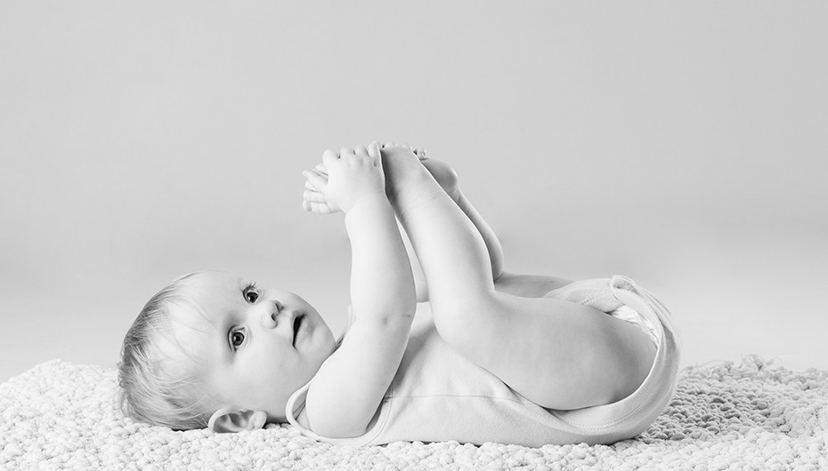 Cute image of baby lying down holding feet in black and white by Emotion Studios. 