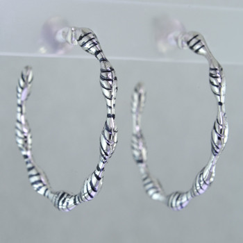 Wear these hoops for day or night. With twisted scallops and black oxidized accents, they'll spice up anything you wear. Perfect with the little black dress. Rhodium plated Sterling Silver. Measure 1/8 inch wide with 1 1/4 inches diameter opening, with posts.

Handcrafted in Northern Spain.