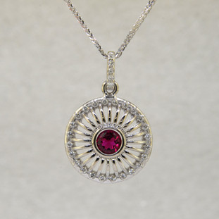 Mixing traditional with modern, this white gold pink tourmaline pendant is sophisticated and classy. Wear it any time, day or night. Crafted in 14 karat White Gold, set with a rich red .50ct. round pink Tourmaline gemstone, and surrounded by .22ct. T.W. of Ideal cut Diamonds. A delicate Diamond bail tops off this beautiful pendant. Includes a .07mm 14 karat White Gold Diamond cut wheat chain, 18 inches long. Measures 1 inch.

Designed, and created in our studio by the artist Stuart J.