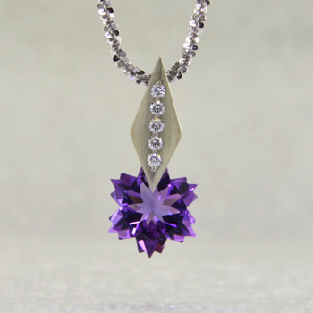 This Amethyst snowflake and Diamond Piercette® pendant will melt your heart. Set in 14 karat white gold, with an 8mm custom cut deep purple Amethyst snowflake, dangling from a kite shaped bail, sprinkled with .05ct. T.W. Ideal cut Diamonds.
The Amethyst snowflake gemstone is custom cut, exclusively for us, in Canada. Includes a 14 karat white gold 1.3mm diamond cut wheat chain, 18 inches long. Pendant measures 5/8" long.
Designed and handmade by the artist Stuart J.

A Piercette® is a patented method of setting, with a gemstone that moves. The gem is set so that it swivels with every movement of the wearer, exhibiting extra sparkle. 