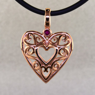 See the excitement on her face when you give her this beautiful vintage heart pendant. Lovely filigree heart in 14 karat rose gold, accented with a deep red genuine ruby. This dynamic heart measures 1 inch long, and hangs on a 2mm black leather cord.

Designed and handmade by the artist Stuart J.